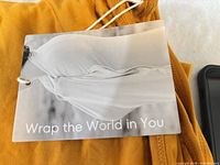 Hangtag reading 'Wrap the World in You' attached to mustard fabric