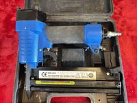 Side view of blue pneumatic stapler in case showing magazine label and overall condition