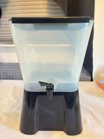 Front view of dispenser showing clear container, black base and spigot