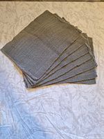 Stack of seven blue placemats showing ribbed texture and fringe.