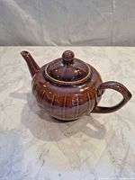 Full view of stoneware teapot showing spout, handle, lid, ribbed body, drip glaze finish