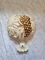 Front view showing cream ceramic wall pocket with gold grape cluster and leaf relief