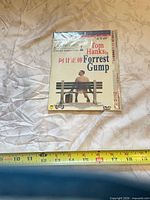 Front of sealed Forrest Gump DVD with Chinese text, showing cover art and NTSC/widescreen markings, tape measure for scale