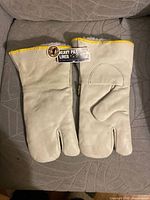Full view of both gloves laid flat showing leather material, yellow trim, tags attached