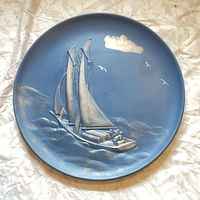 full front view of round blue ceramic plaque showing sailboat design