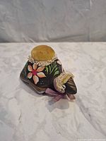 Oblique view of ceramic pincushion showing front velvet pad, floral painting and ribbon