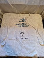 full view white apron with bilingual text, pocket logos, straps visible
