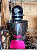 Full view of black KitchenAid Artisan mixer with stainless bowl on shelf