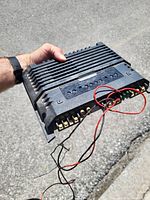 Top view of black 4-channel car amplifier showing heat-sink fins, terminal blocks, and attached wiring