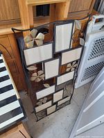Full view of black metal wall photo frame showing decorative gold leaves and nine cream fabric photo openings
