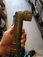 Side view of Fulton olive drab right-angle flashlight showing lens bezel, belt clip, and body markings