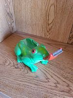 Side view of green resin frog figurine showing red metal tongue cigarette rest and paint chips