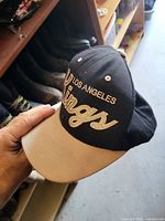 Top and front view of black cap with off-white brim and embroidered Los Angeles Kings logo