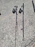 Two assembled spinning rod and reel combos laid on pavement with third rod section alongside