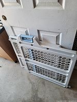 Folded white and gray plastic pressure-mounted baby gate leaning against a door