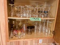 Cabinet showing two shelves filled with assorted wine glasses, tumblers and shot glasses