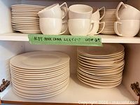 Front view of two shelves showing stacks of white Aldy plates and cups