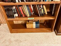 Overall view of wooden bookcase with books on middle shelf and dictionary on bottom shelf