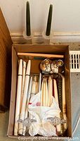 Box containing assorted taper candles and visible candle holders