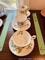 Three of the teacup and saucer sets lined along green arrow