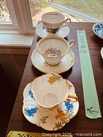 Three stacked teacup and saucer sets showing assorted patterns and gilt detailing