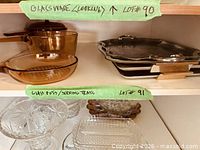 Shelf with two amber glass Visions saucepans and three stacked stainless steel serving trays
