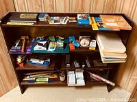 Full view of wood bookcase loaded with assorted office supplies across four shelves