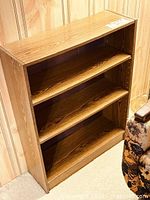 Front angled view of laminate wood-grain bookcase showing two adjustable shelves and fixed base