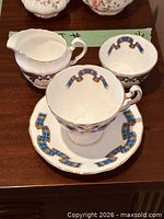 Teacup on saucer with creamer and sugar bowl displaying pattern and gold trim