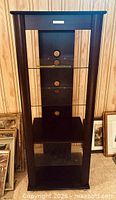 Full front view of Bell'Ogetti stand showing wood frame, three glass shelves, bottom wood shelf, and brand badge
