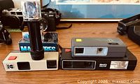 Three cameras with flash cubes and flash attachment on table