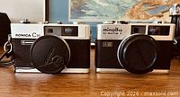 Front view of both Konica C35 Automatic and Minolta Hi-Matic F cameras with lens caps
