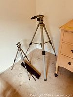 Both tripods standing next to dresser and wall