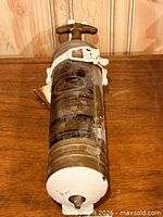 Full view of Pyrene brass fire extinguisher lying on wood surface