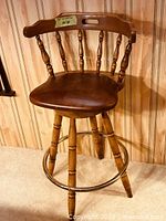 Full view of wooden swivel bar stool showing seat, backrest, legs, and brass foot ring