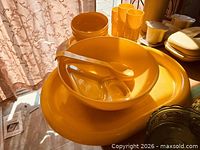 Yellow plastic bowls, platter, tumblers and utensils on table under sunlight