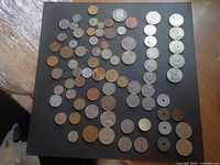 Full spread of approximately 70 mixed world coins laid out on black board