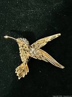 Front view of gold tone hummingbird brooch with rhinestones