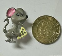 Mouse brooch beside Chuck E. Cheese token for scale