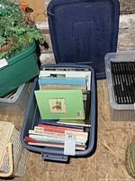 Blue plastic bin filled with books sitting among other storage bins