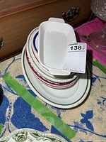 Stack of various vintage white hotel ware dishes with colored rims on dresser