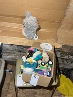 Box on chair containing teal Furby, small plush, toy tractor, misc. figures