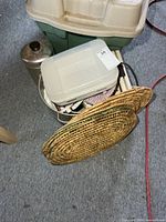 Stack of items including plastic container, woven placemats, stainless canister, glimpse of sandwich maker cord