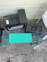 Overview showing three black toolboxes and green folding stool on ground