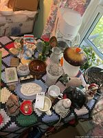 assorted household items on crocheted cloth showing canister, coffee maker, vases, bowls and figurines