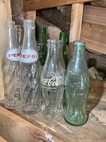 Front view showing two Pepsi spiral bottles, clear Coca-Cola ACL bottle, green Coca-Cola bottle, and two green Wilson's bottles behind