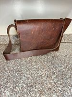 Front view of brown leather messenger bag showing flap and strap