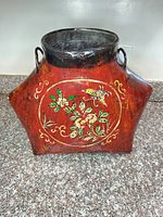 Front view of red papier-mâché vase with floral painting and side handles