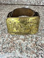 Front view of brass buckle on leather belt showing raised Jeepers Jamboree design and text