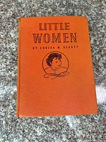 Front cover of orange clothbound Little Women showing title and portrait vignette